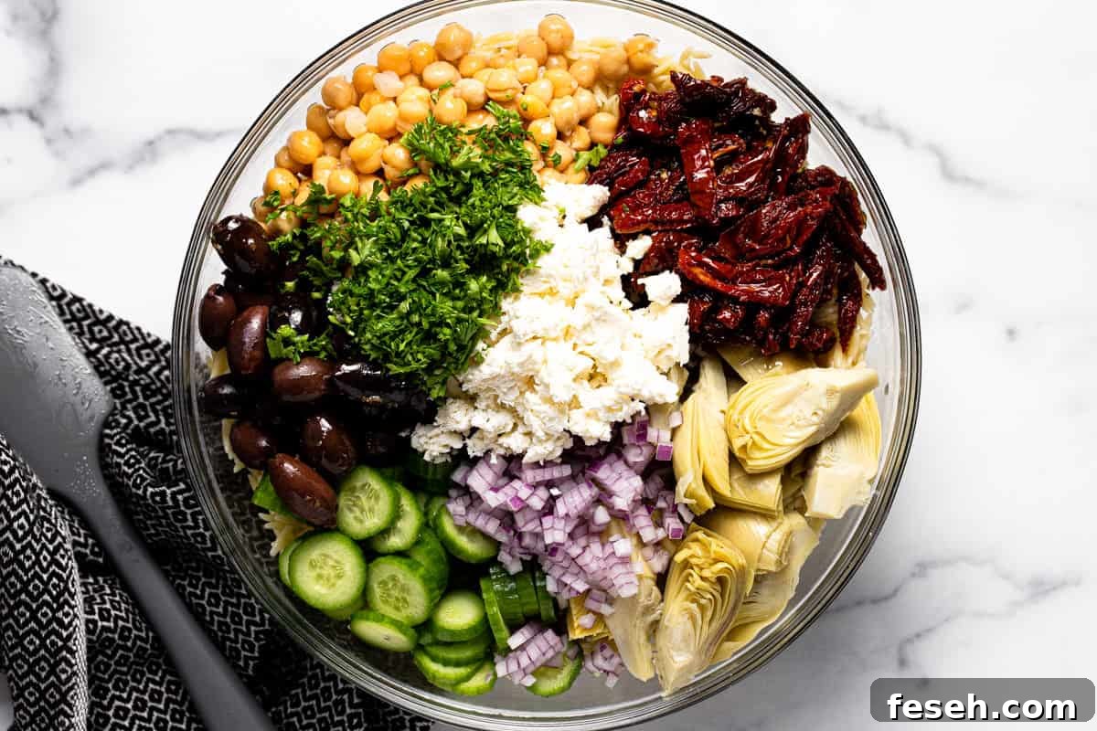 Glass bowl filled with ingredients to make Mediterranean pasta salad