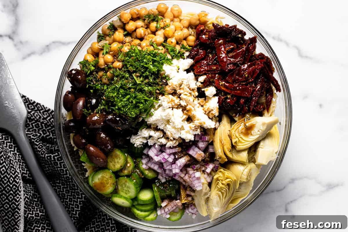 Glass bowl filled with ingredients to make Mediterranean pasta salad