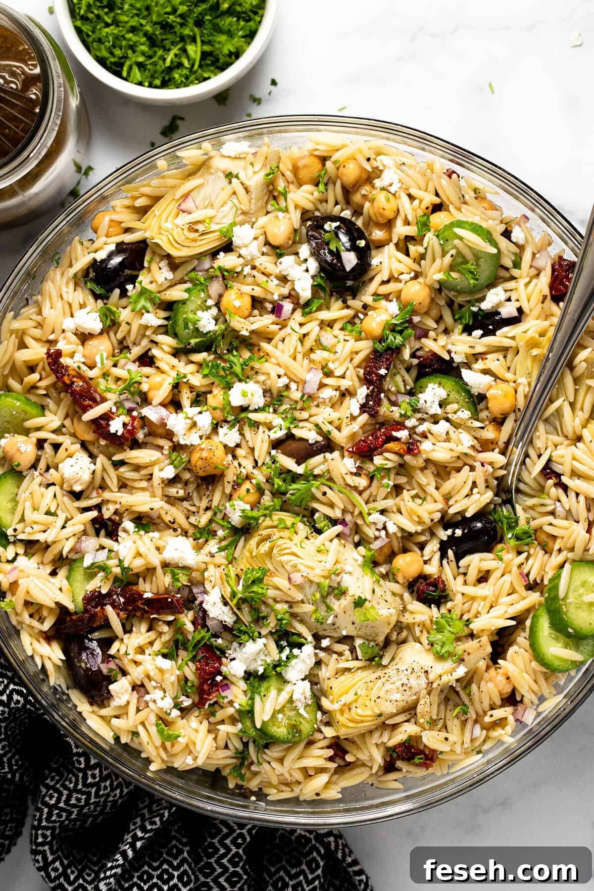 Large glass bowl filled with Greek pasta salad garnished with parsley 