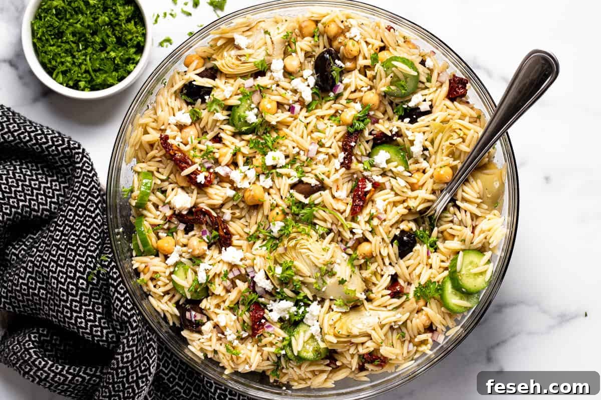 Large glass bowl filled with Greek pasta salad garnished with parsley 