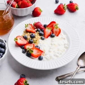 Cottage cheese, blueberries, strawberries and granola in a white bowl with a drizzle of honey.