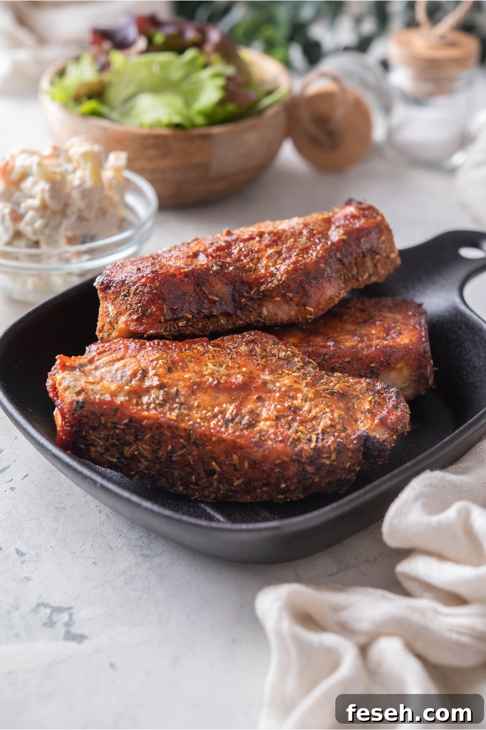 A stack of three seasoned barbecue pork ribs on a black plate.