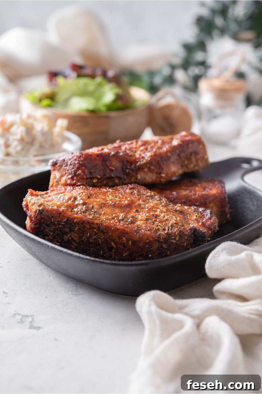 A stack of three seasoned barbecue pork ribs on a black plate.