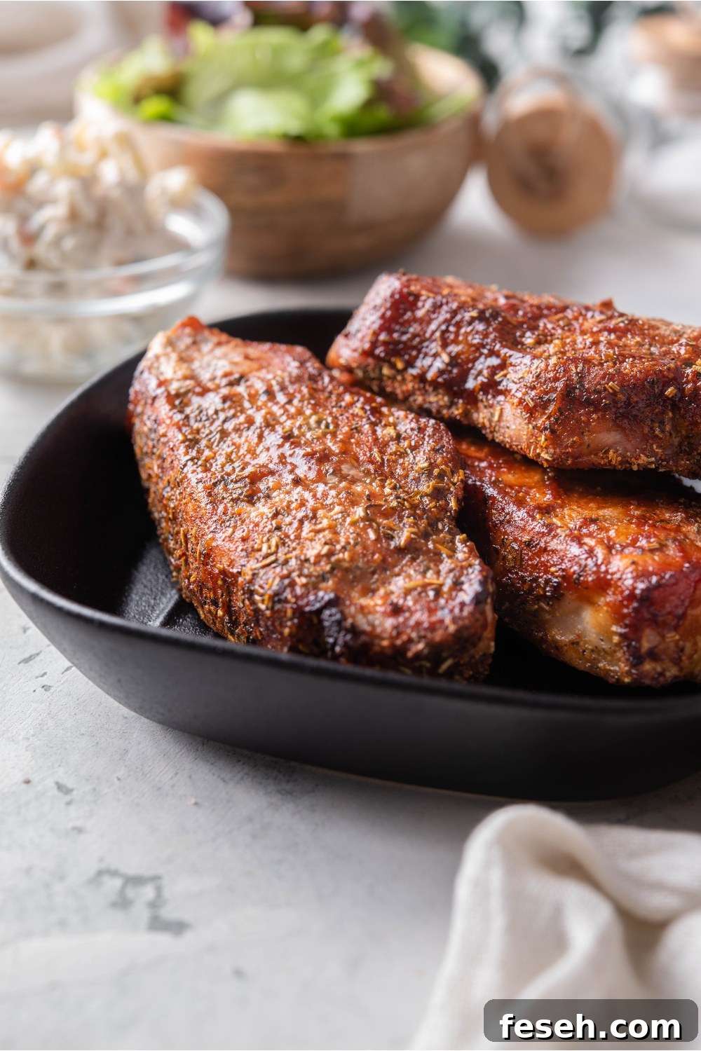 A stack of three seasoned barbecue pork ribs on a black plate.