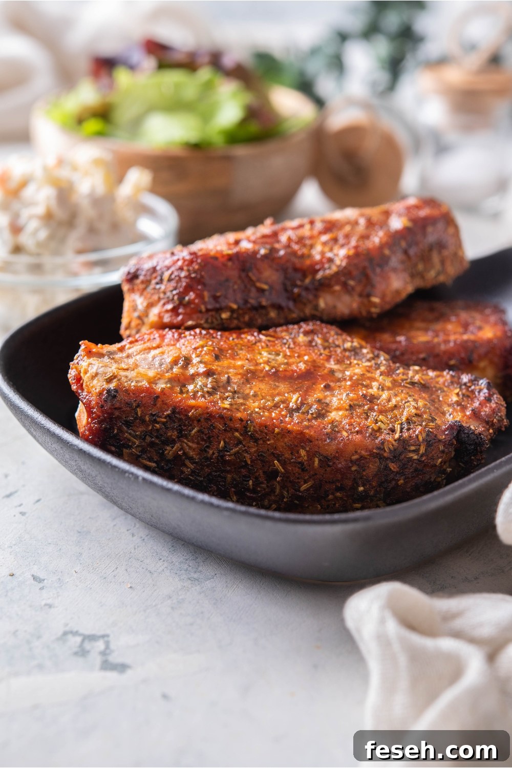 A stack of three seasoned barbecue pork ribs on a black plate.