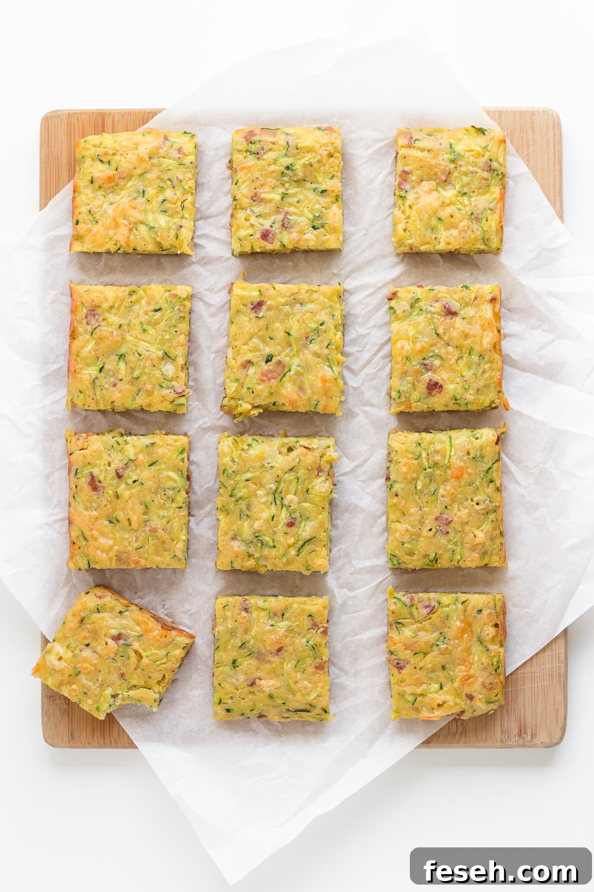 Square cut up pieces of zucchini slice on a wooden board lined with parchment paper.