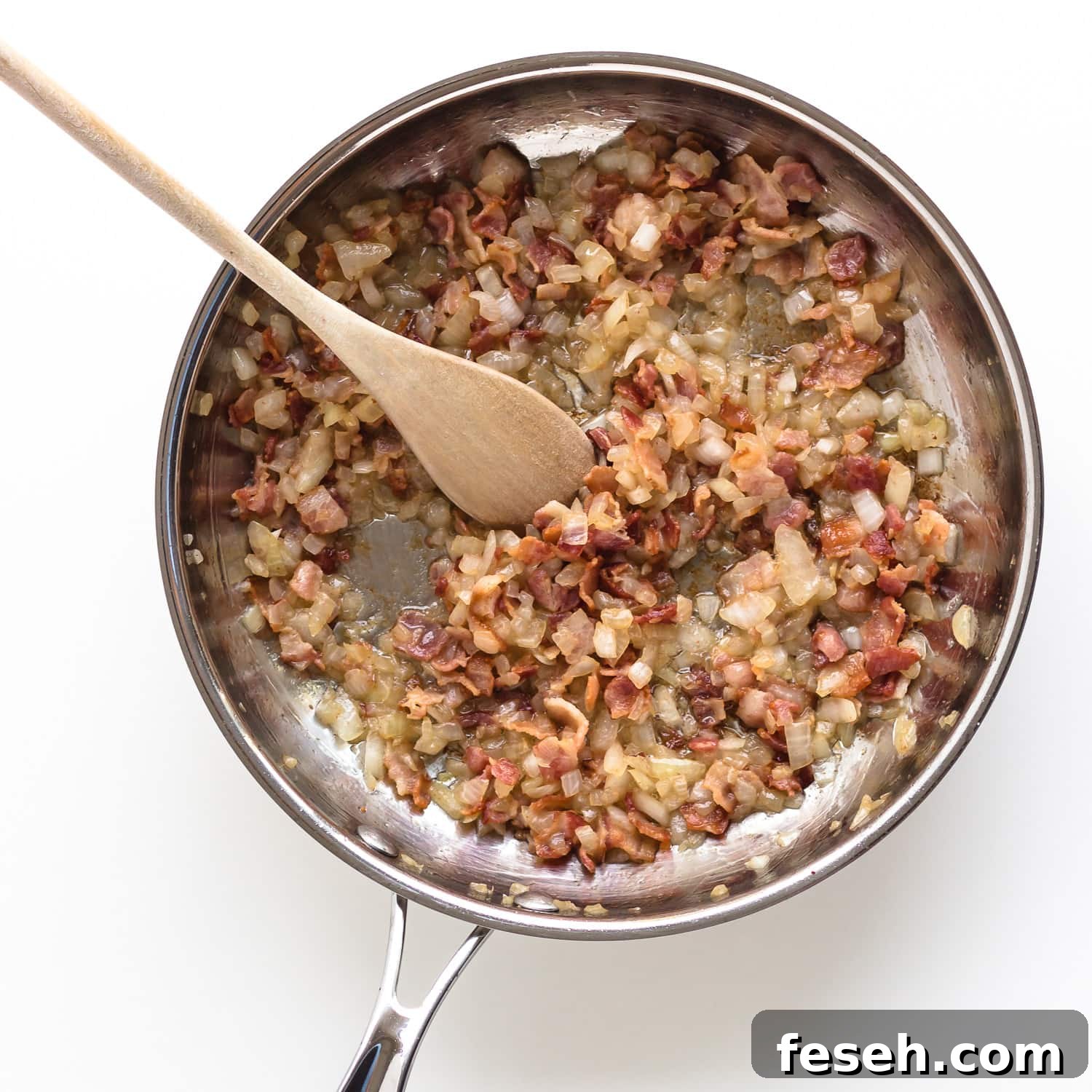Sautéed bacon and onions in a stainless steel frying pan.