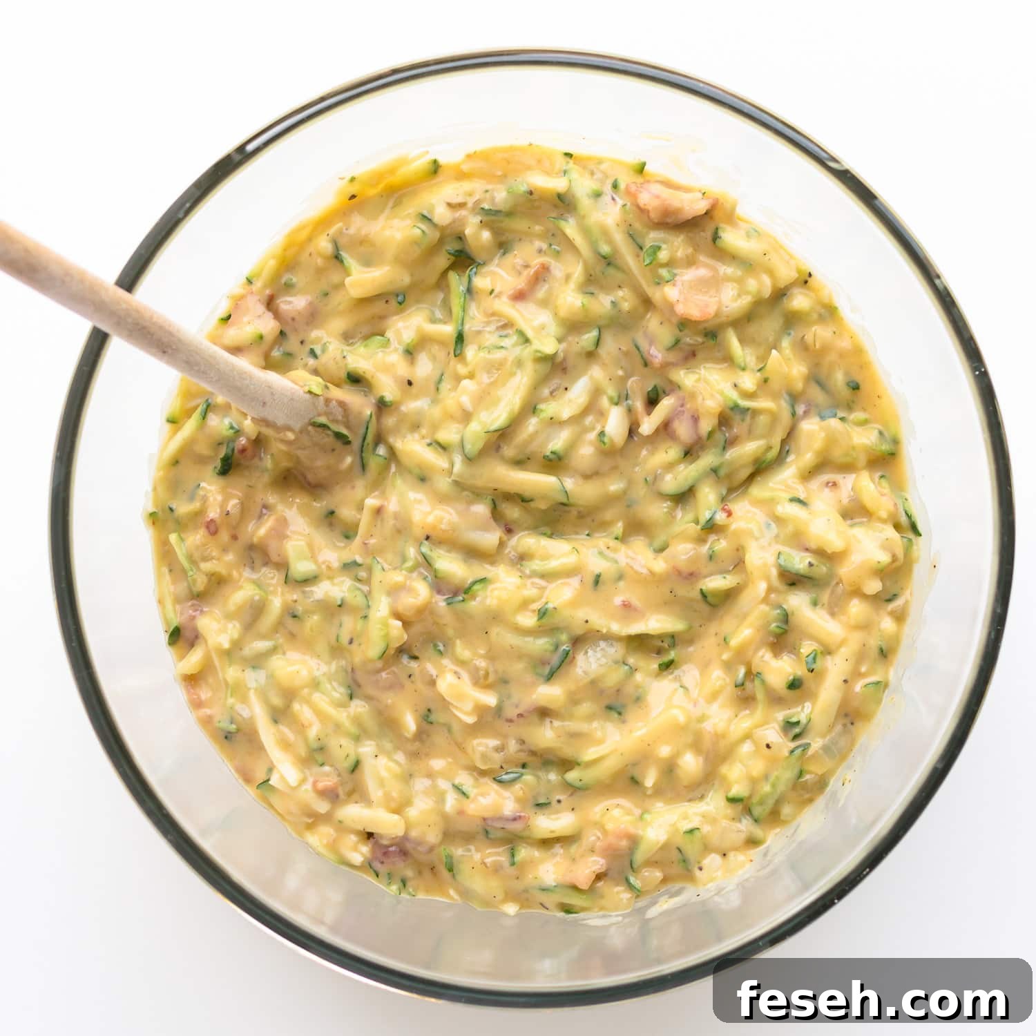 Zucchini slice batter in a glass mixing bowl with wooden spoon.