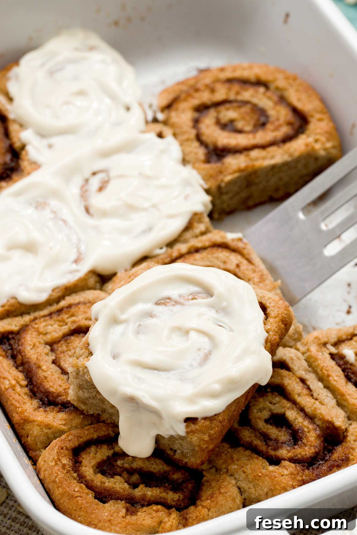 A close-up of a pan of gluten-free cottage cheese cinnamon rolls with a maple cream cheese spread on top.