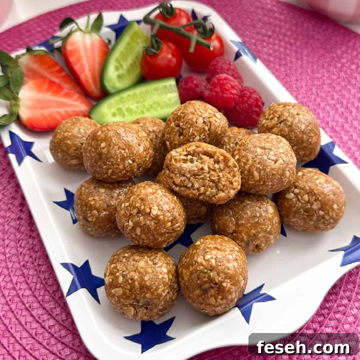 A pile of Biscoff Oat Energy Bites served on a white tray with a blue star pattern, along with fresh, chopped berries and cucumber.