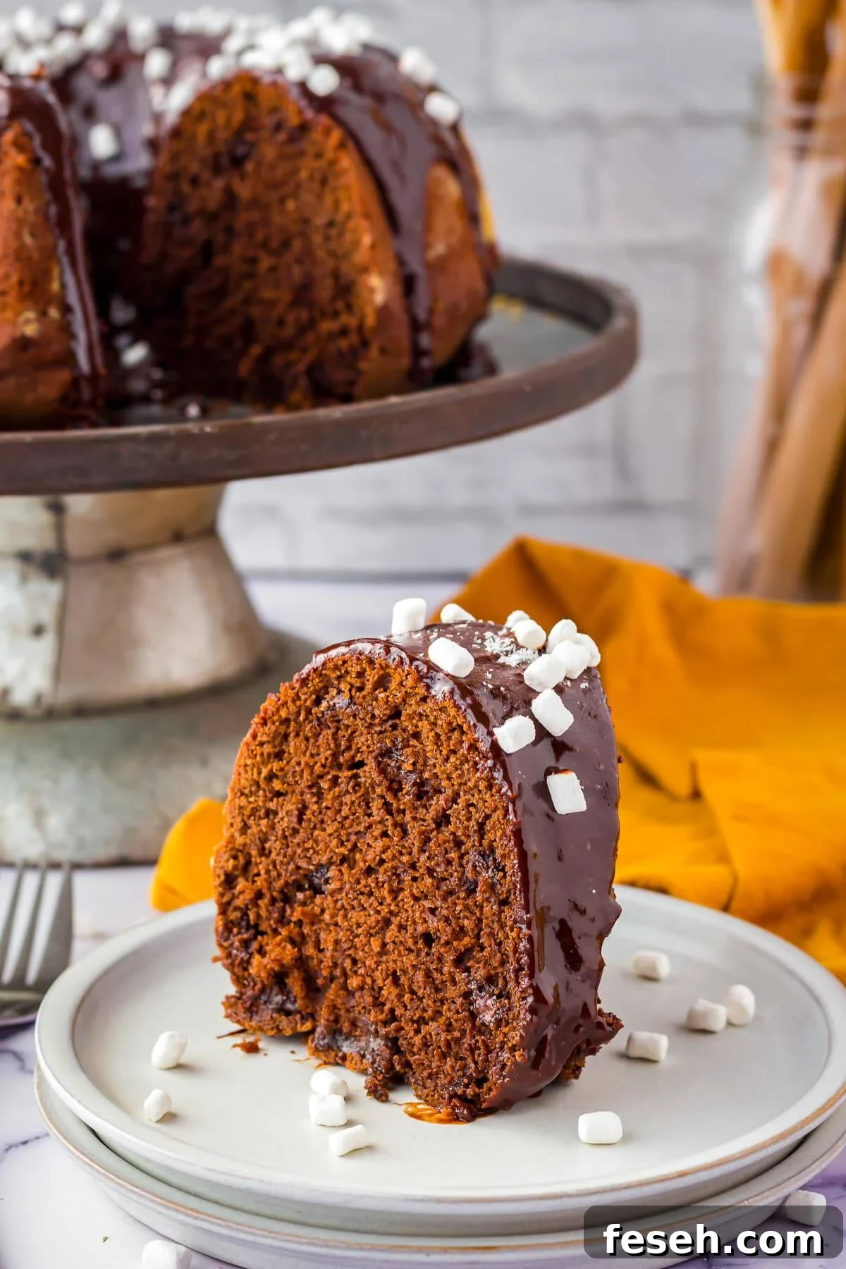 One slice of Hot Chocolate Cake on white plate with mini marshmallow bits on plate and on top of cake.