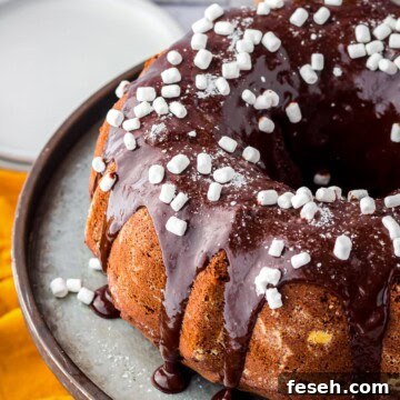 Finished Hot Chocolate Cake on metal cake stand with glaze and mini marshmallow bits.