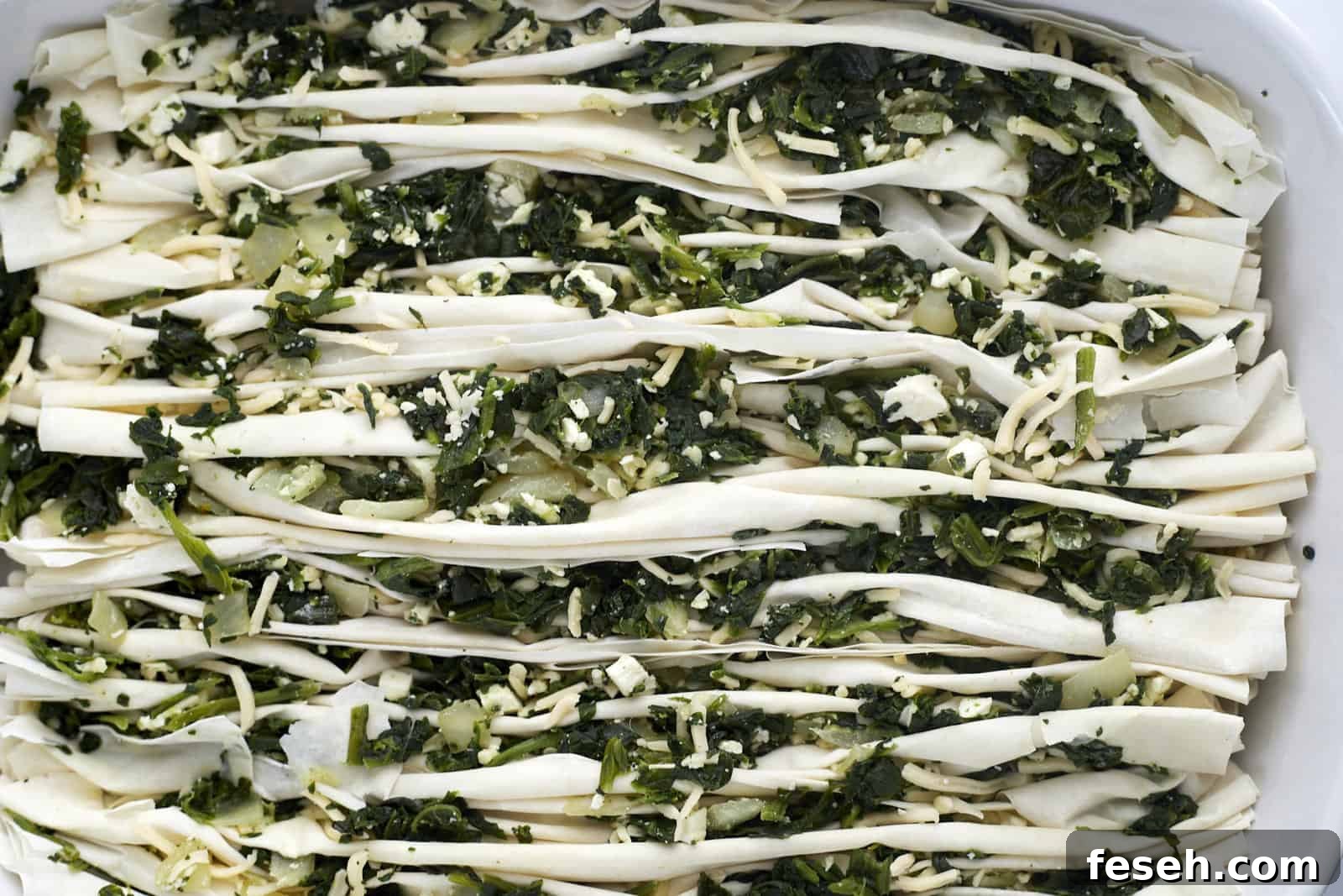 crinkle phyllo dough stuffed with spanakopita filing in a baking dish.