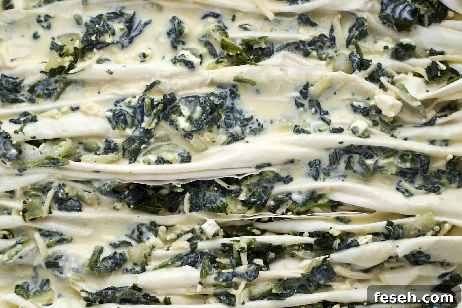 crinkle phyllo dough stuffed with spanakopita filing in a baking dish topped with a milk and yogurt mixture.