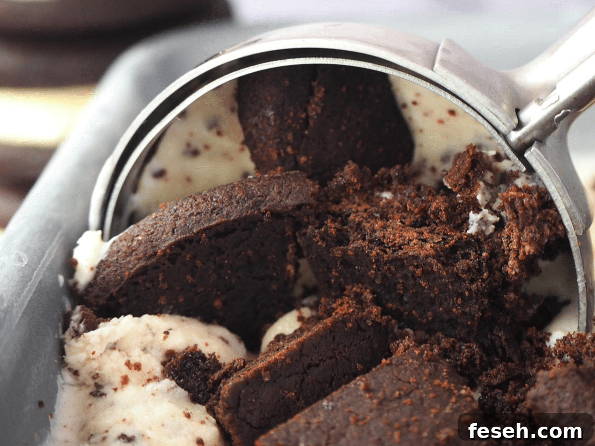 Close up scooping cookies and cream ice cream in loaf pan, with Oreos in the background.