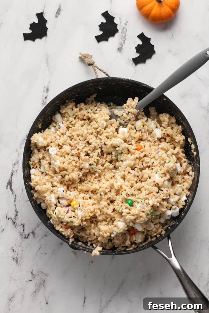 Halloween rice krispie treats being mixed with a spatula in a saucepan