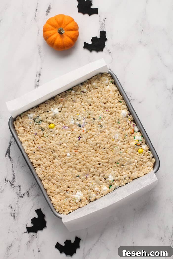 Unfrosted halloween rice krispie treats in a parchment-lined metal pan