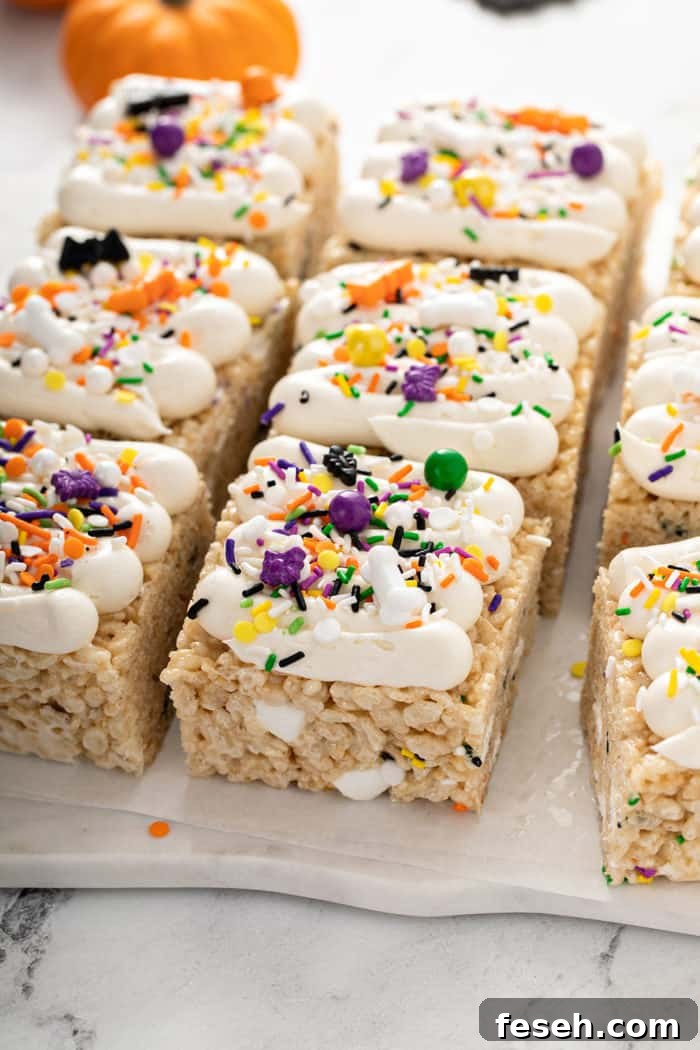 Frosted Halloween rice krispie treats topped with Halloween sprinkles on a piece of parchment paper