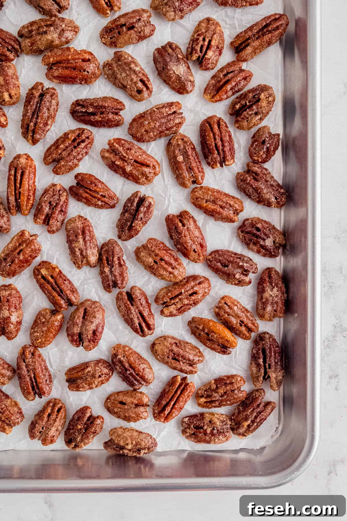 candied pecans on a piece of white parchment paper on a baking sheet