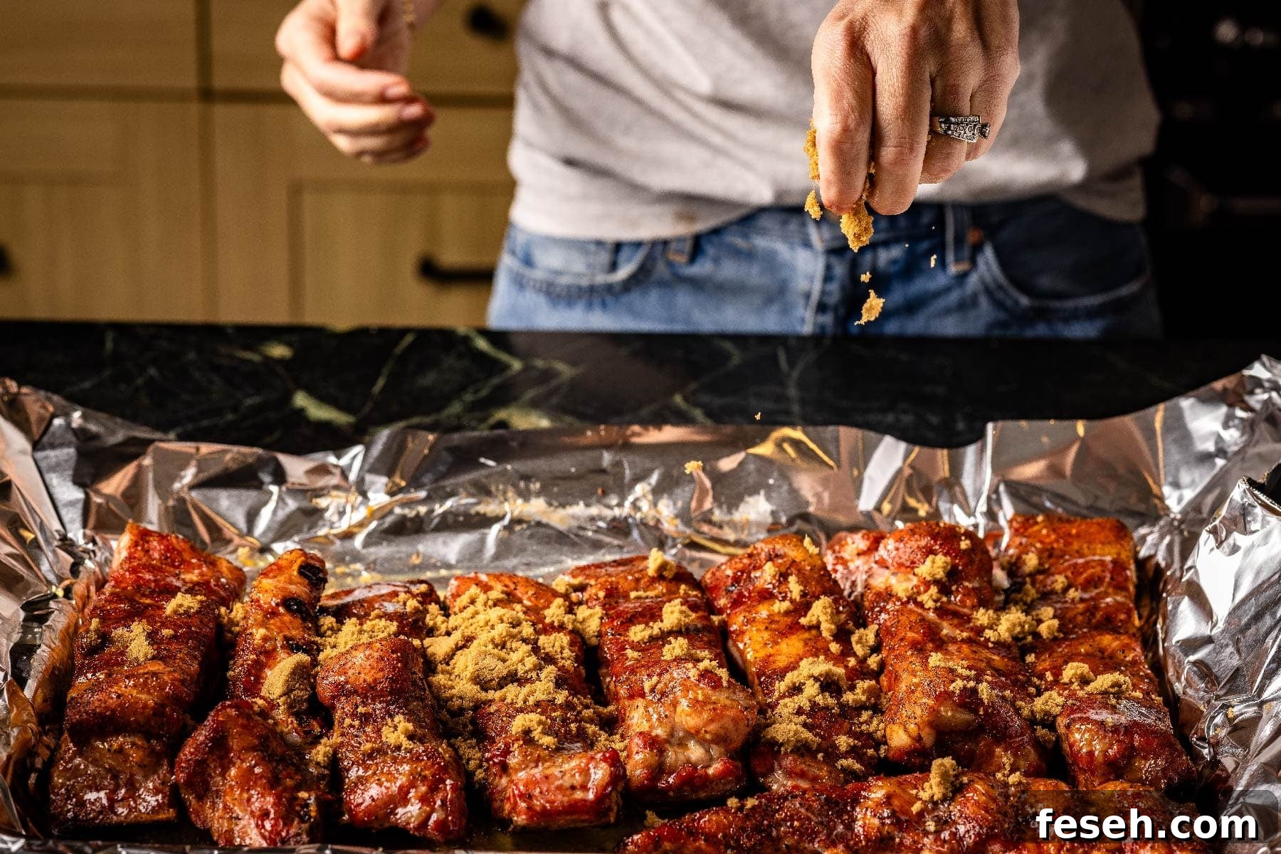 Smoked ribs in foil being sprinkled with brown sugar.