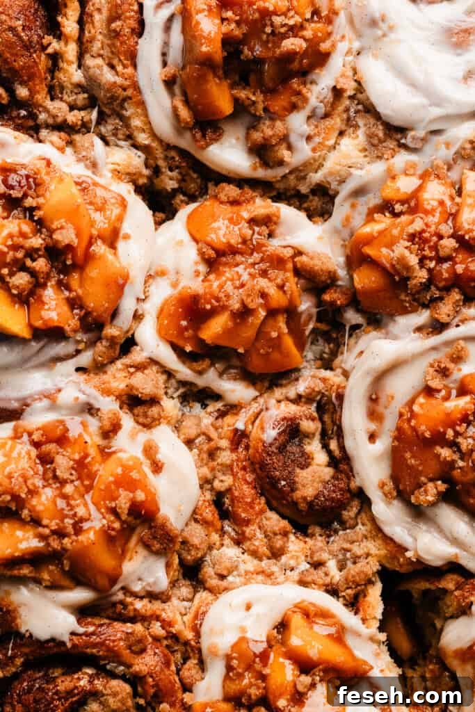 A bird's eye view of the pan of cinnamon rolls topped with cream cheese frosting, peach filling, and crumble.
