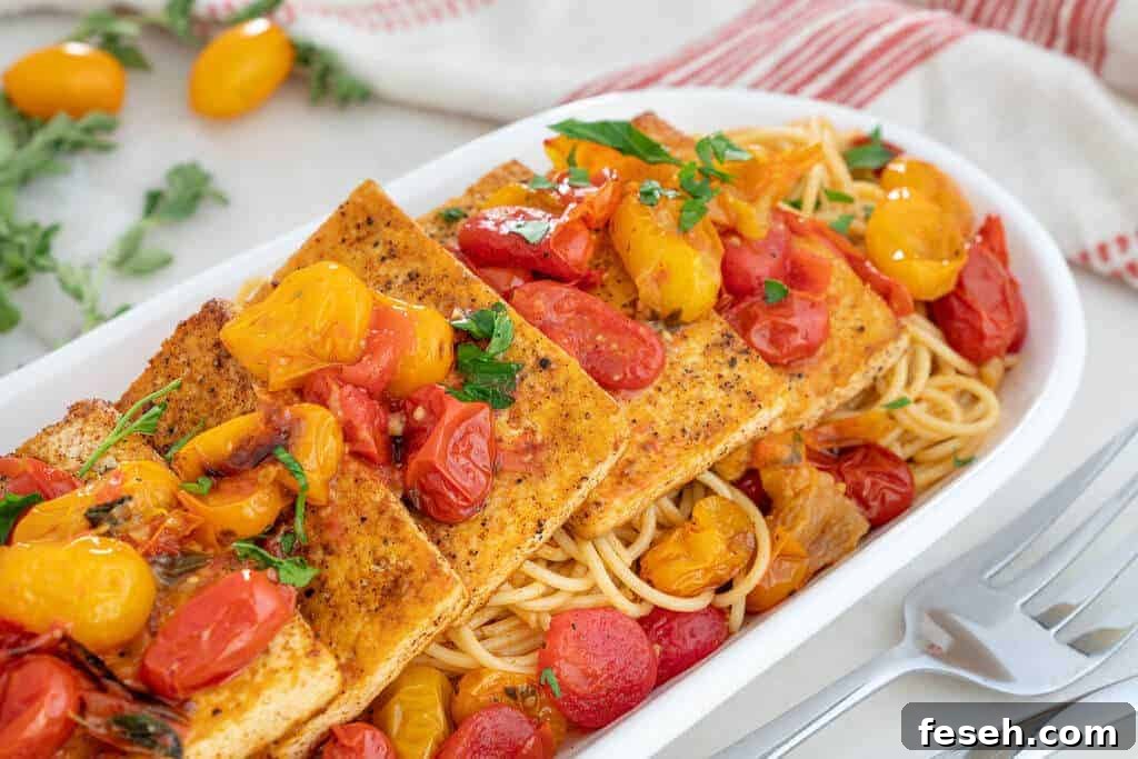 Tofu filets over spaghetti and cherry tomatoes in a long white dish.