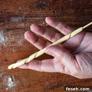 Dough wound around a bamboo skewer being displayed on an open hand.