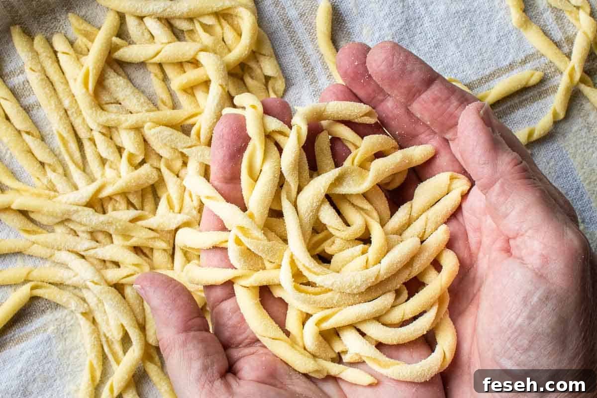 Pile of twirled, handmade pasta in cupped hands with more pasta nearby.