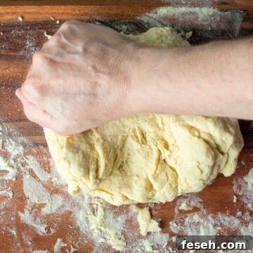 A hand kneading yellow pasta dough.
