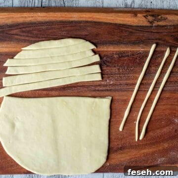 Oblong sheet of rolled dough cut into thick strips with three strands of dough nearby.