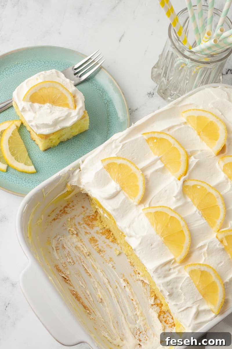 Overhead view of lemon poke cake in baking dish with serving of lemon cake in the background.
