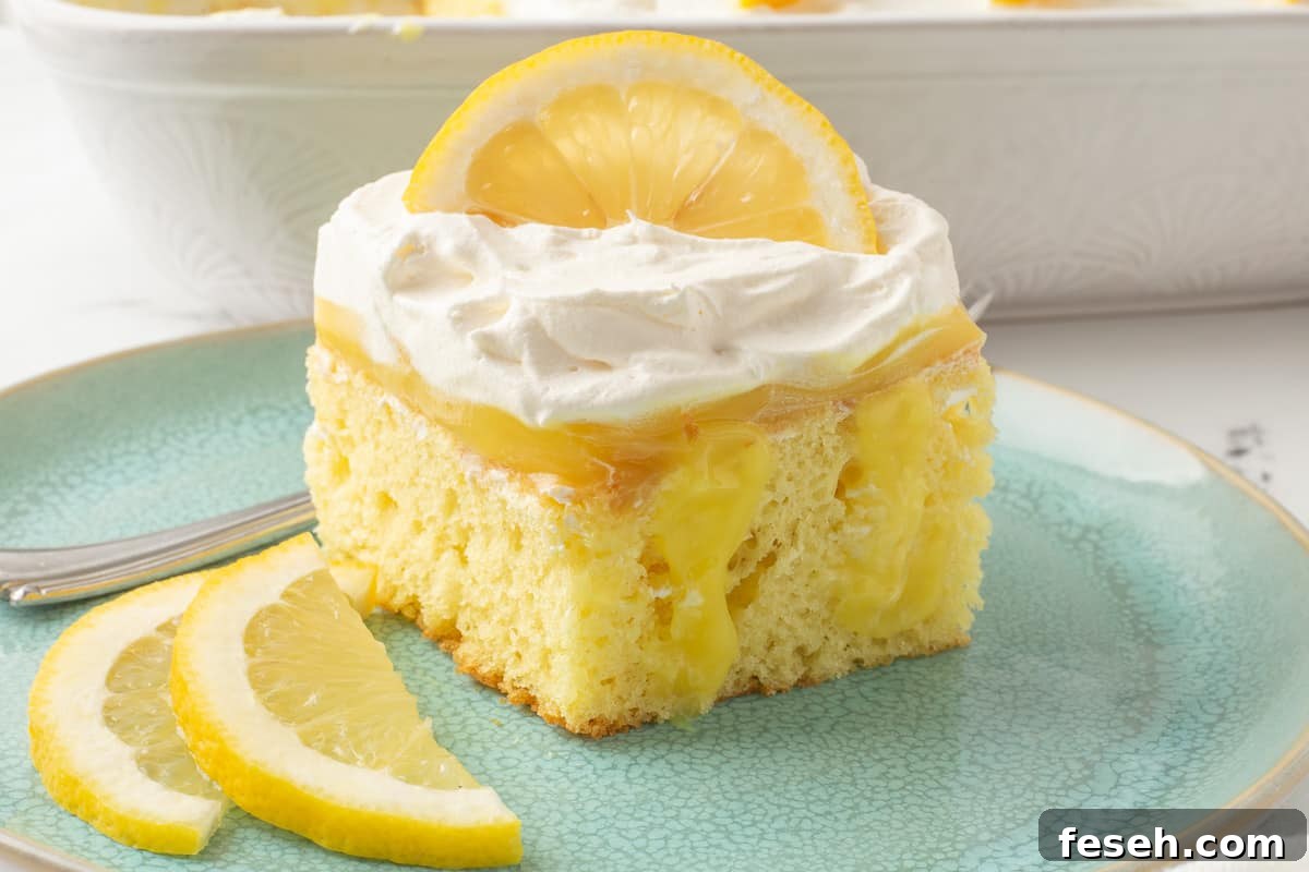 Serving of lemon poke cake on a plate with sliced lemons and a fork.