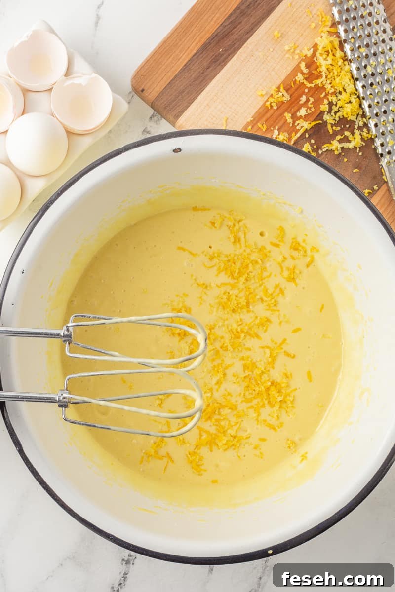 Cake mix with lemon zest in mixing bowl with hand mixer.