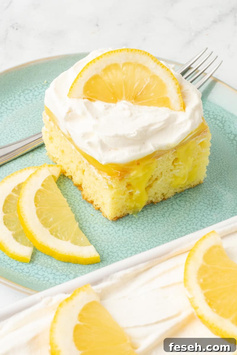 Sliced of lemon pudding poke cake on an aqua plate with sliced lemons and a fork.