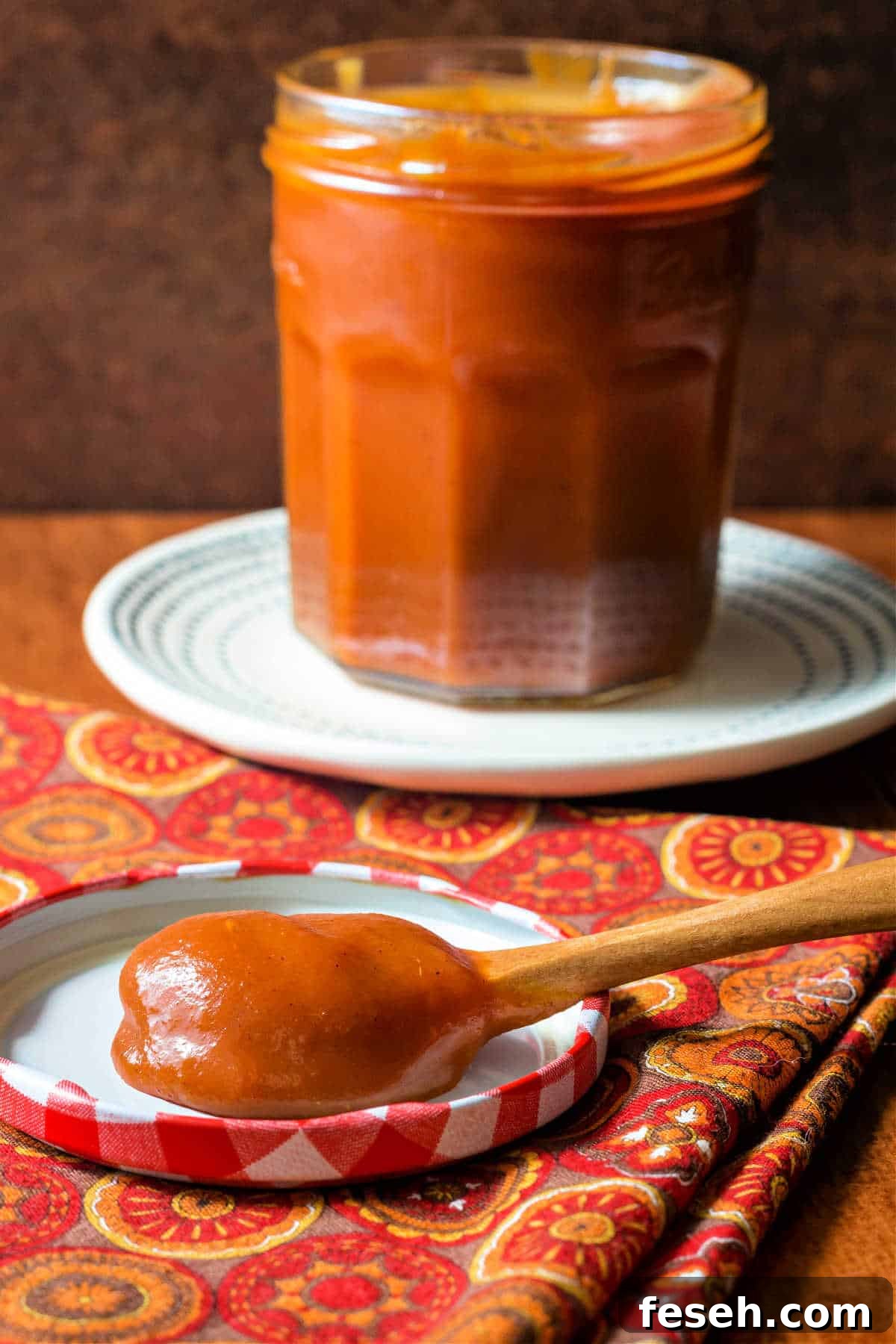A full jar of deep amber caramel sauce with a spoonful of the sauce resting on the lid of the jar.