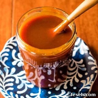 A jar of deep orange-amber sauce on a blue patterned plate.