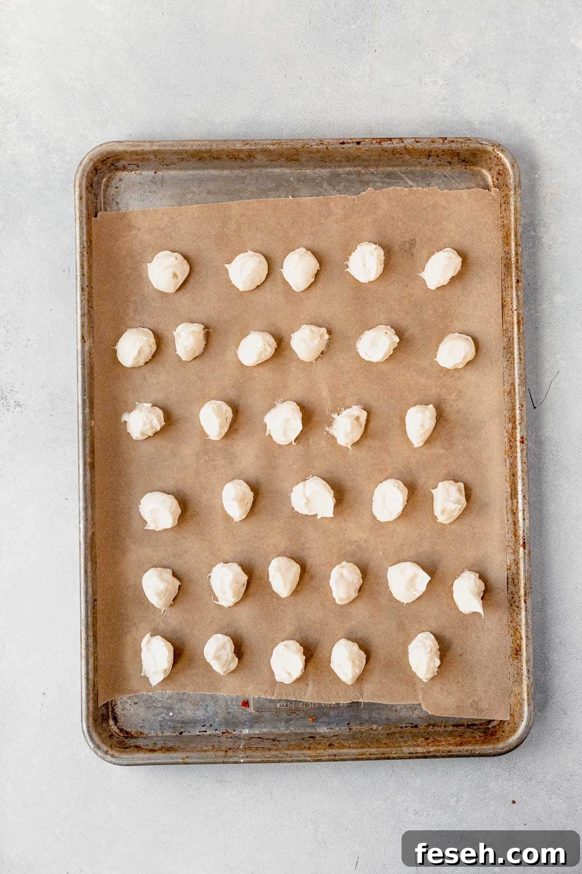 balls of frosting for caramel cheesecake cookies dropped on a sheet of parchment paper on a baking sheet.