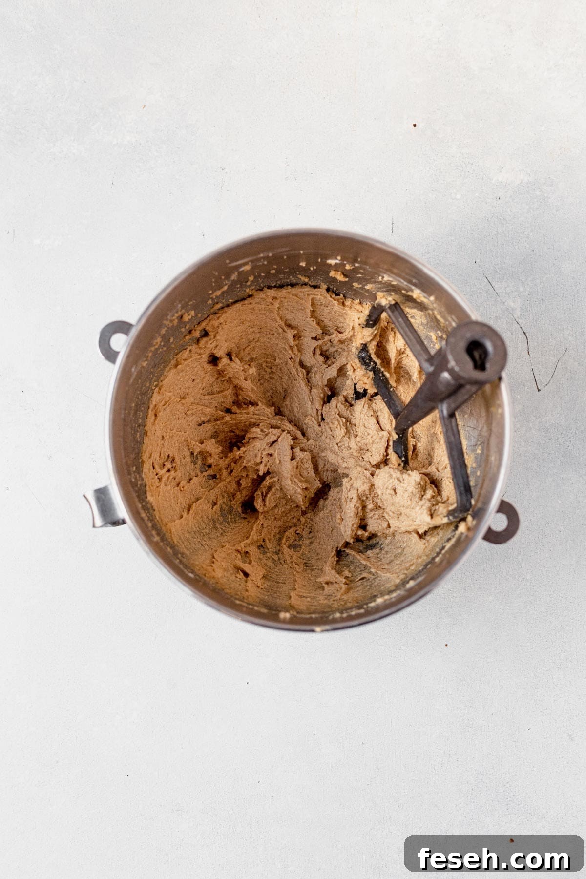 dough for caramel cheesecake cookies mixed together in a bowl with a paddle attachment.