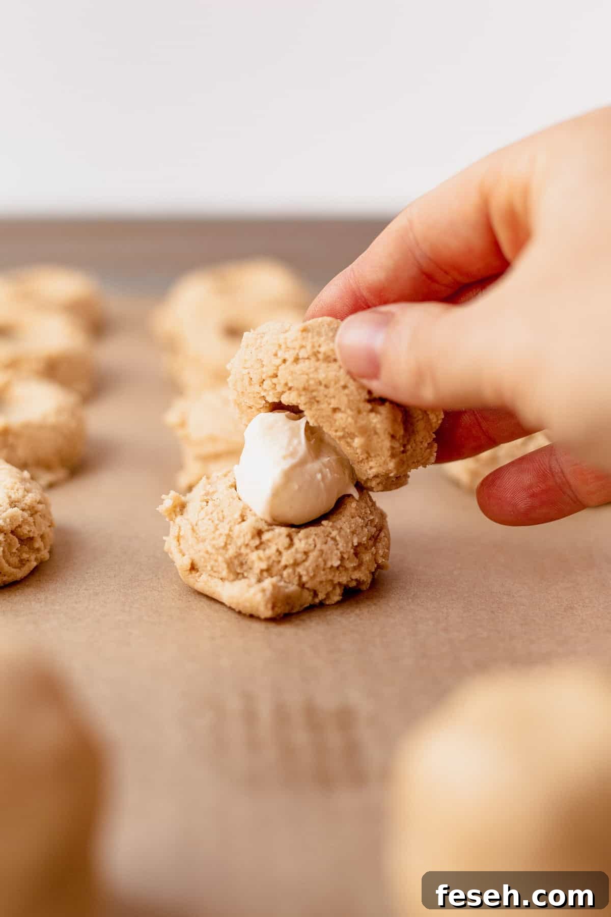 tops and bottoms of caramel cheesecake cookie dough being sandwiched together with a ball of icing in the middle.