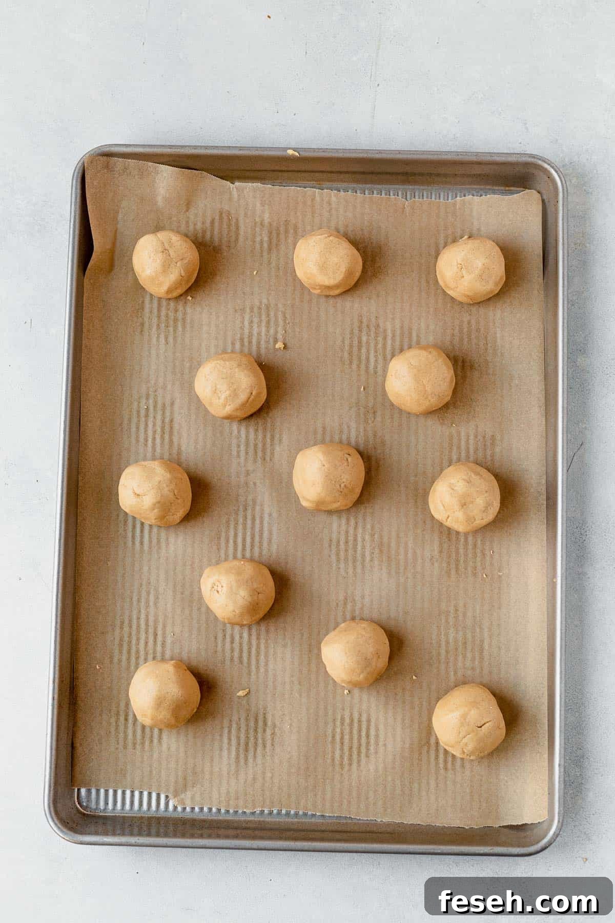 balls of caramel cheesecake cookie dough with icing in the middle resting on a baking sheet waiting to be baked.