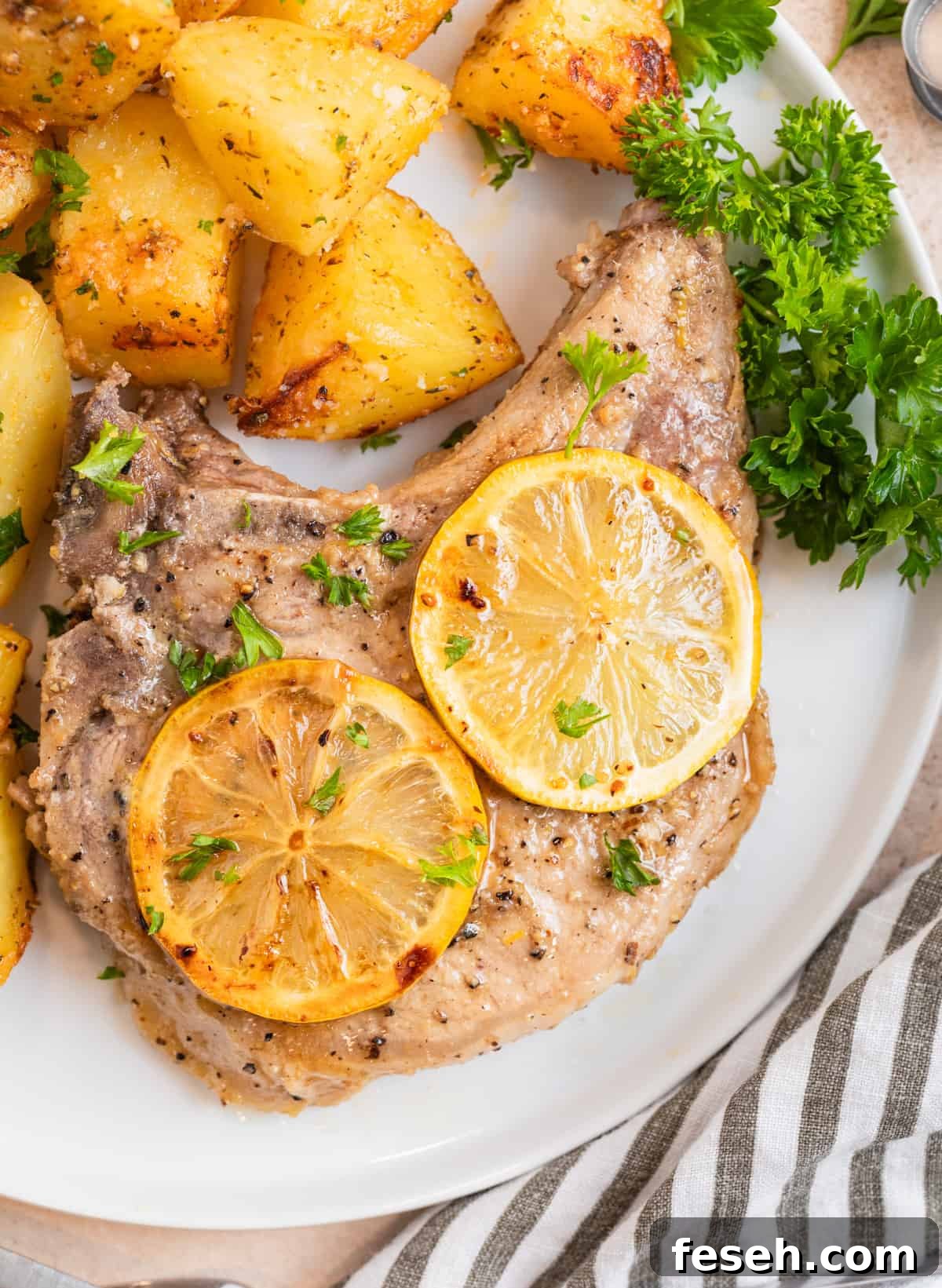Lemon pepper pork chop on white plate with parsley and potatoes.