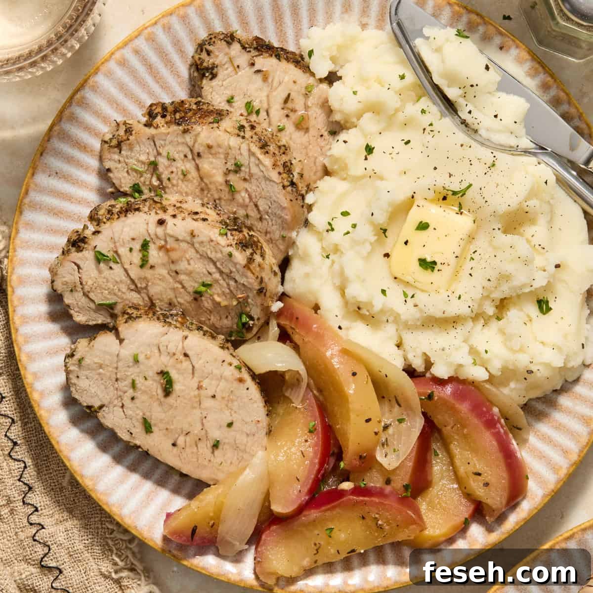 Pork tenderloin sliced on plate with apples and mashed potatoes.