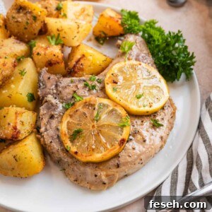 Lemon pepper pork chop on white plate with lemon slices and freshly chopped parsley.