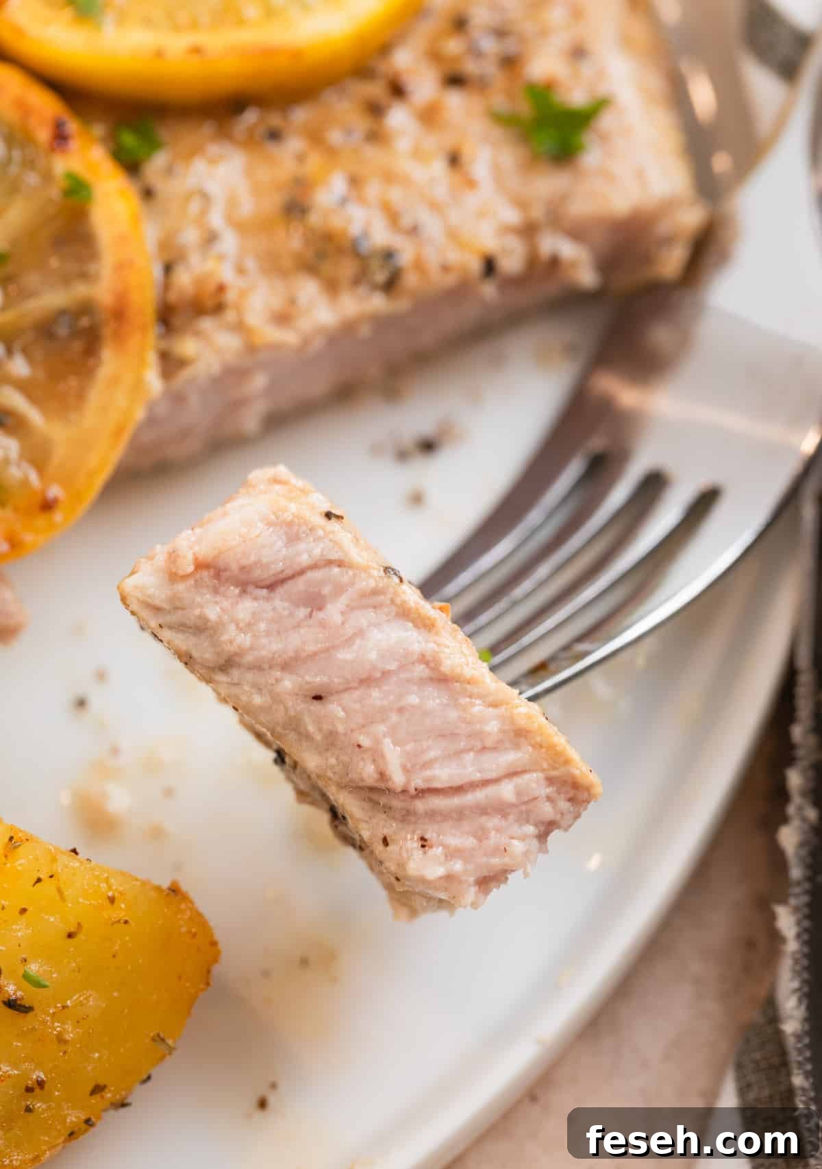 White plate with piece of lemon pepper pork chop on fork.