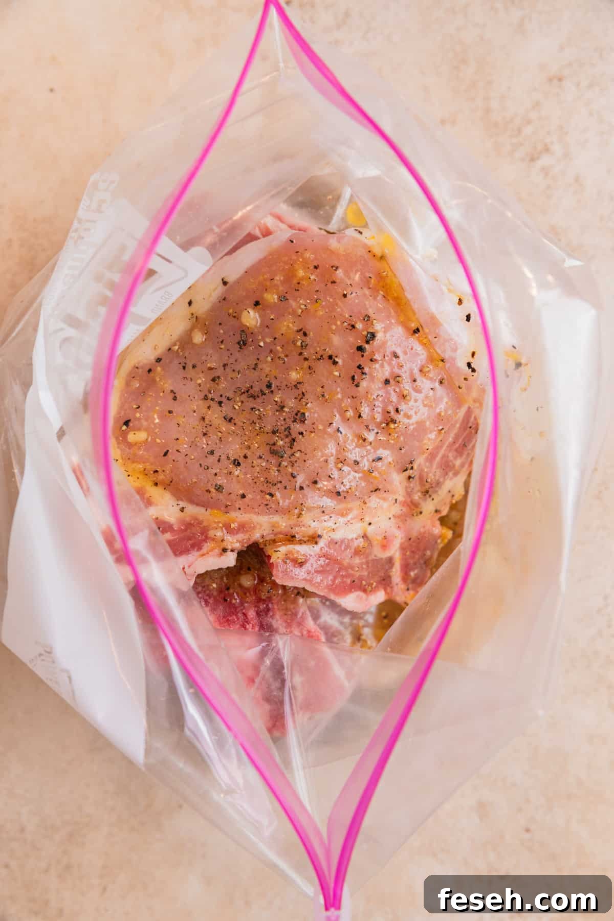 Raw pork chops in plastic bag with lemon pepper marinade over top.