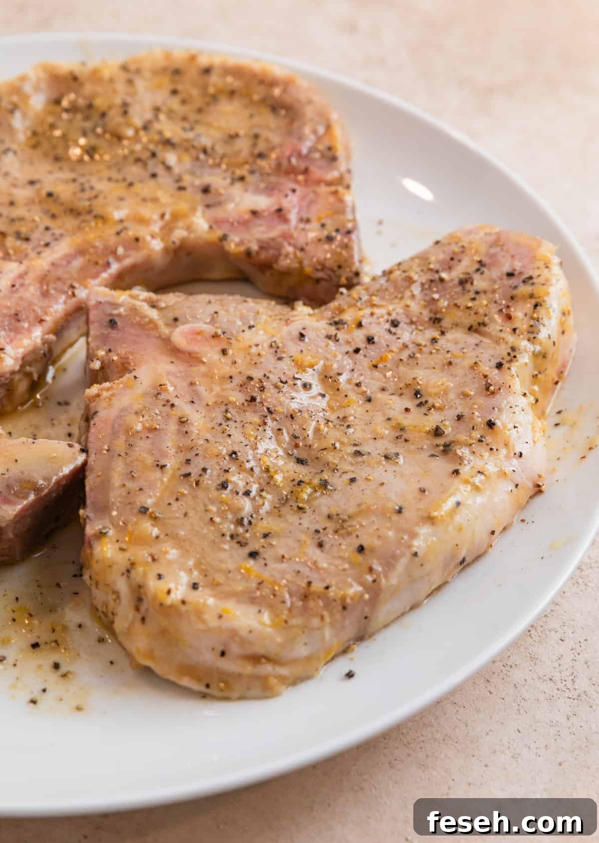 White plate with marinaded lemon pepper pork chops before cooking.