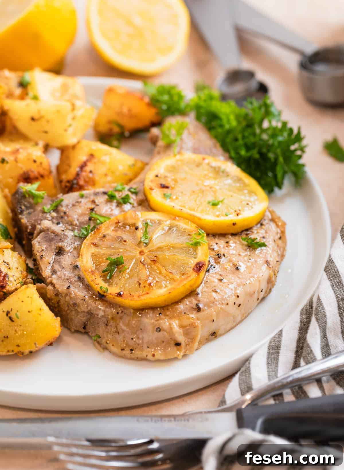 Pork chop and potatoes on white plate with parsley and sliced lemons over top.