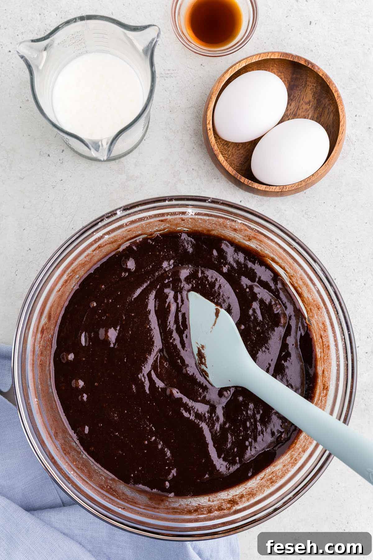 Chocolate cake batter in a bowl with eggs, milk, and vanilla extract on the side. 