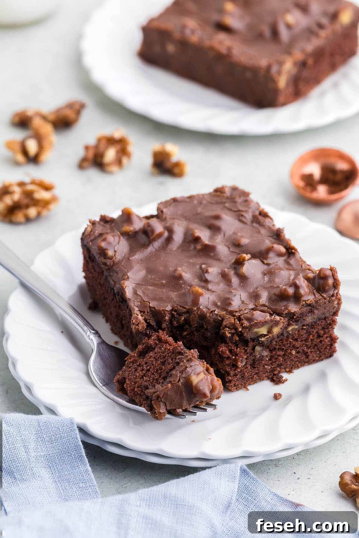 A slice of chocolate sheet cake on a white plate with a fork. 