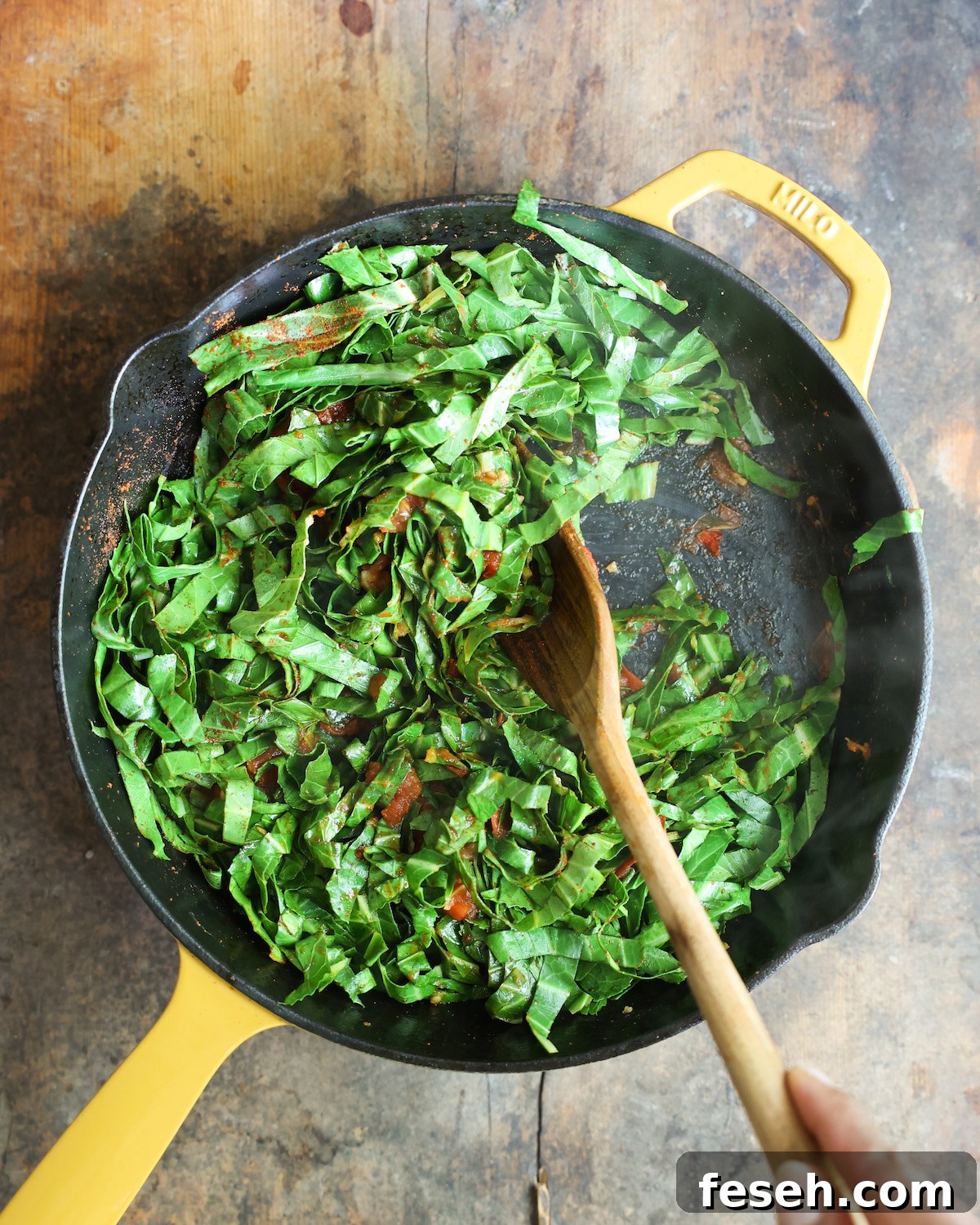 Bright green collard greens sautéing in a yellow skillet.
